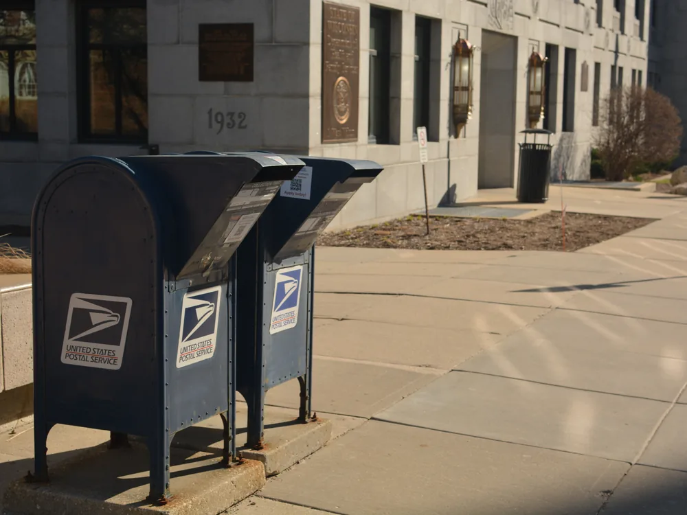 A blue post-office collection mailbox on a downtown sidewalk